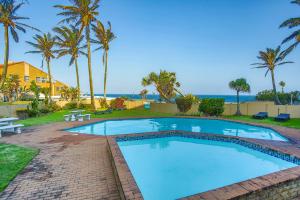 a swimming pool with palm trees and the ocean at 10 Coral Cove Beach Lodge in Ballito