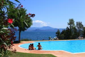 a group of people sitting around a swimming pool overlooking the water at Campeggio Villaggio San Giorgio Vacanze in Manerba del Garda