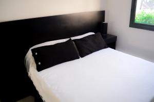 1 dormitorio con cama blanca y almohadas negras en Complejo Azul Marino en Villa Gesell