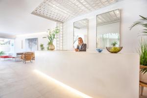 une femme est assise au comptoir dans une pièce avec des plantes dans l'établissement Grupotel Picafort Beach, à Can Picafort