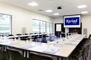 una grande stanza con tavoli, sedie e schermo di Kyriad Hotel Laval a Laval
