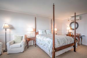 a bedroom with a four poster bed and a chair at Wades Point Inn on the Bay in Saint Michaels