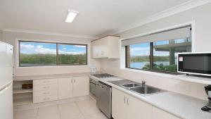a kitchen with white cabinets and a sink and two windows at Kingscliff Waters Apartment 5 in Kingscliff