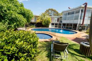 einen Pool in einem Garten mit einem Stuhl und einem Gebäude in der Unterkunft Jacksons Motor Inn in Adelaide