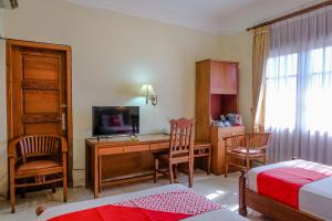 een slaapkamer met een bed en een bureau met een televisie bij Super OYO 1803 Hotel Sarangan Permai in Madiun