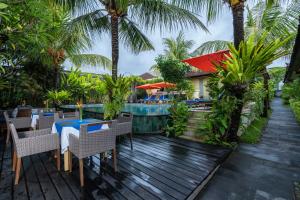 a wooden deck with tables and chairs and a swimming pool at Natya Hotel Tanah Lot in Tanah Lot