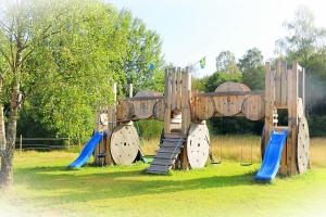 een houten speeltuin met een glijbaan en schommels bij Hagbards By Gårdspensionat in Slöinge