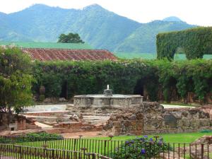 a garden with a fountain with mountains in the background at Hotel Museo Spa Casa Santo Domingo in Antigua Guatemala