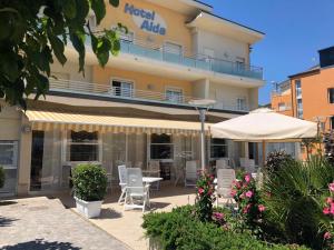 Cet hôtel possède une terrasse avec des chaises et un parasol. dans l'établissement Hotel Alda, à Cervia