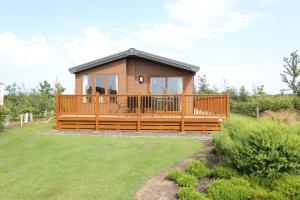 a small cabin with a large deck in a yard at Cosy Dreams Lodge in Beal