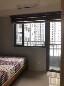 een slaapkamer met een bed en een groot raam bij Grass Residences Tower 5 in Manilla