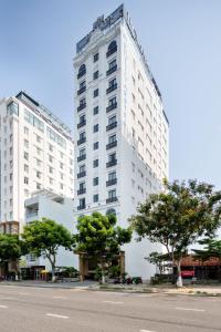 a tall white building with trees in front of a street at Roliva Hotel & Apartment Danang in Da Nang