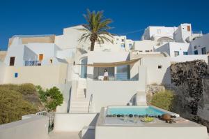 a white house with a swimming pool and a palm tree at Aesthesis Boutique Villas Fira in Fira