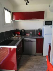 una pequeña cocina con armarios rojos y fregadero en Charmant studio bord de mer, en Ouistreham