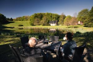 a man and a woman sitting at a table by a lake at Klærke Hostel in Skanderborg