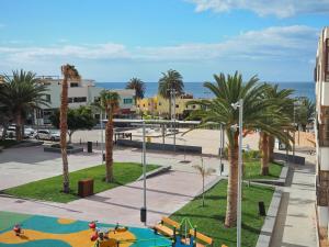 un parque con parque infantil y palmeras en FeWo Flamingo - Morro Jable Fuerteventura, en Morro del Jable