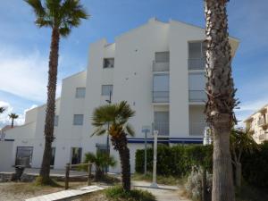 een wit gebouw met palmbomen ervoor bij Le Sud sur Plage in Mèze