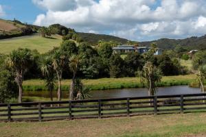 a fence next to a river with palm trees at Pukeko Nest in Russell