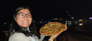 Una donna con gli occhiali che tiene una pizza grande di Varah Square Guest House a Pushkar