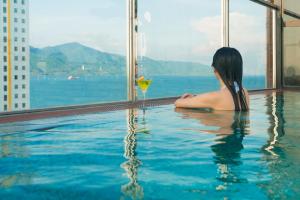 a woman sitting in a swimming pool with a drink at Sofiana My Khe Hotel & Spa- Rooftop Pool Bar in Danang