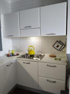 La cocina está equipada con armarios blancos y fogones con tetera amarilla. en Michi's Home - Attico in Centro, en Bari