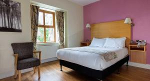 
a bedroom with a bed, chair, lamp and window at The Coach House Hotel in Oranmore

