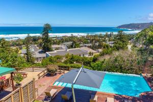 an outdoor swimming pool with an umbrella and the beach at Under the Boardwalk B&B Guest House in Wilderness