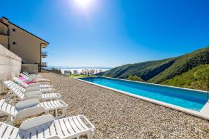a row of white lounge chairs next to a swimming pool at Pansion Villa Betina in Lovran