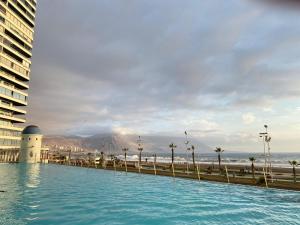 a swimming pool next to a building and the ocean at Condominio Mar Egeo Iquique in Iquique