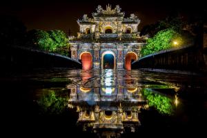 a building with a reflection in the water at night at The Times Hotel in Hue