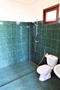 Baño de azulejos verdes con aseo y lavamanos en Main Reef Guest House en Hikkaduwa
