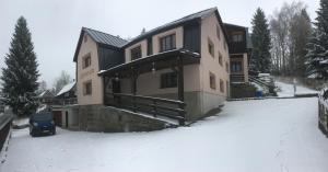 a house in the snow with a blue car in front at Penzion Diana in Bedřichov