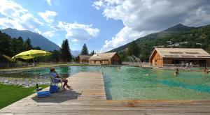 a person sitting under an umbrella next to a swimming pool at Très bel appartement pied de pistes 6 pers Serre Chevalier Chantemerle in Saint-Chaffrey