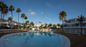 una gran piscina con palmeras y un edificio en Fuentepark Apartamentos, en Corralejo