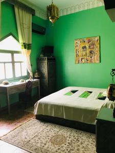 1 dormitorio con paredes verdes, 1 cama y 1 mesa en Le Petit Riad Maison d'hôtes, en Ouarzazate