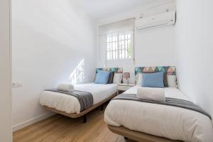 Habitación con 2 camas, paredes blancas y suelo de madera. en Justino Triana Central by Valcambre, en Sevilla