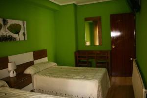 a green bedroom with two beds and a mirror at Hotel Restaurante Valdevenados in Anguiano