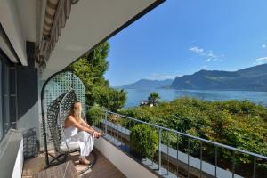 a woman sitting on a balcony looking out at the water at Seehotel Pilatus in Hergiswil