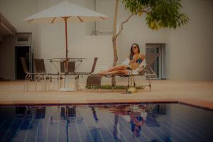 a woman sitting in a chair next to a swimming pool at Ipê Palace Hotel in Adamantina