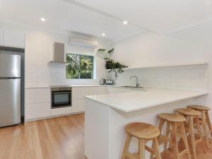 a white kitchen with a counter and stools at Byron Beachside 8 in Byron Bay