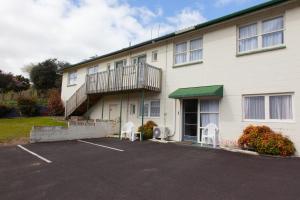 a building with a balcony and two chairs in a parking lot at Otorohanga & Waitomo Motels in Otorohanga