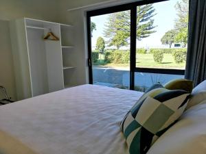 Waikanae Beach Ocean View Apartments في جيسبورن: غرفة نوم بسرير ونافذة كبيرة