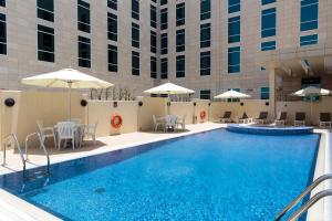 una piscina de hotel con mesas, sillas y sombrillas en Premier Inn Doha Education City, en Doha