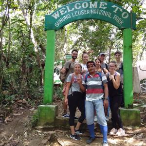 un gruppo di persone che si trovano sotto un cartello verde di Jungle treking & Jungle Tour if you want to stay here,you must book treking only with us a Bukit Lawang