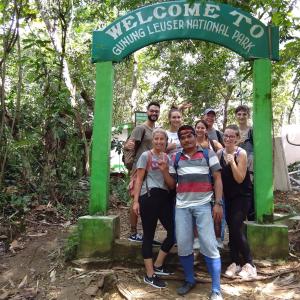 un grupo de personas de pie bajo una señal verde en Jungle treking & Jungle Tour booking with us en Bukit Lawang