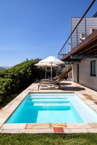 a swimming pool with an umbrella and a house at Cliff Lodge in Gansbaai