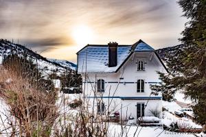 a white house in the snow with the sun behind it at La demeure des tisserands in La Bresse