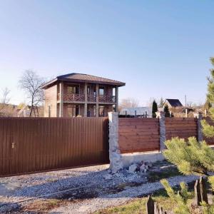 a house behind a fence with a house in the background at Ранчо, Дом для релакса в окружении леса и озёр in Kolonshchina