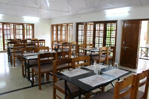 een eetkamer met tafels, stoelen en ramen bij KTDC Kumarakom Gateway Resort in Alleppey