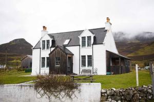 a white house on a hill with mountains in the background at Quaraing House in Staffin